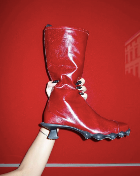 A hand holding a shiny red boot against a red background.